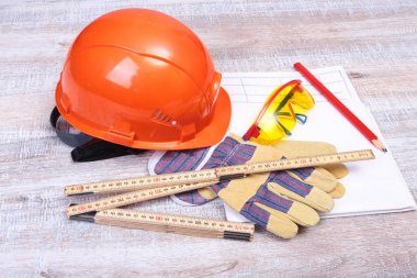 Turuncu kask, koruyucu gözlük, eldiven ve ahşap arka plan üzerinde ölçüm bandı.