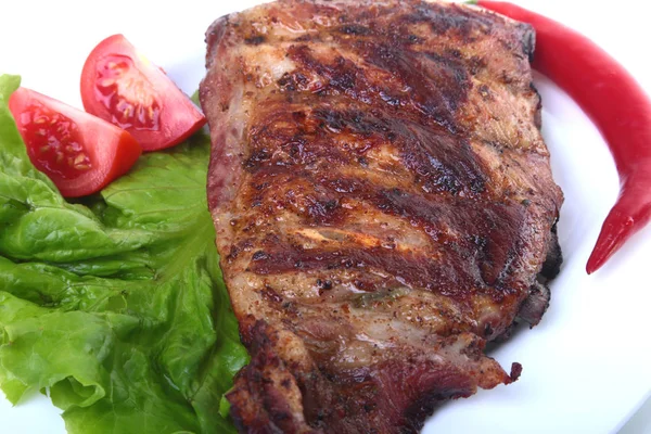 Rusuk babi di panggangan dan cabai dengan tomat, daun selada di piring putih — Stok Foto