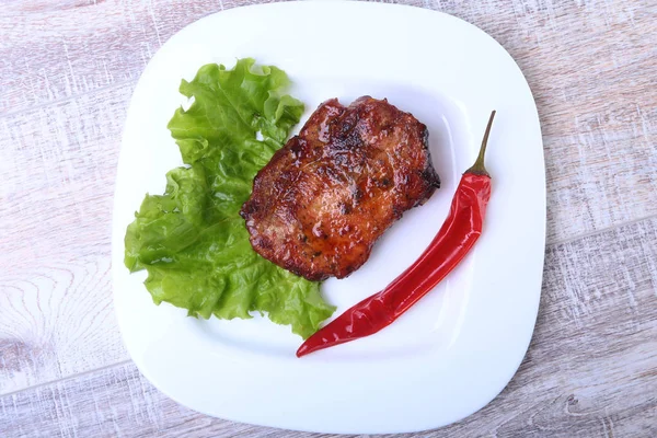 Steak of grilled meat and chili pepper with tomato, lettuce leaves on white plate. — Stock Photo, Image