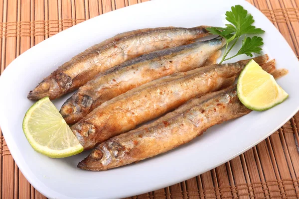 Küçük balık capelin ve beyaz tabakta dilimlenmiş limon kızartma derin. Bira için iyi snack.