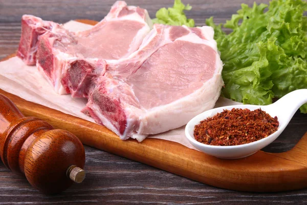 Surový Vepřový steak s kořením listy salátu na dřevěném prkénku. Připraven k vaření. — Stock fotografie