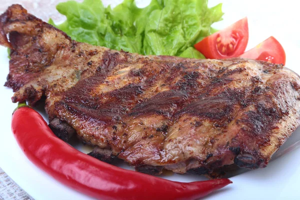 Côtes de porc sur gril et piment avec tomate, feuilles de laitue sur assiette blanche — Photo