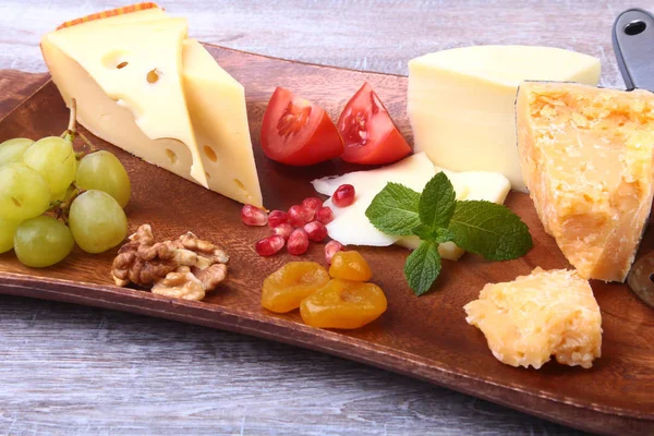 Assortiment van kaas met fruit, druiven, noten en kaas mes op een houten dienblad. — Stockfoto