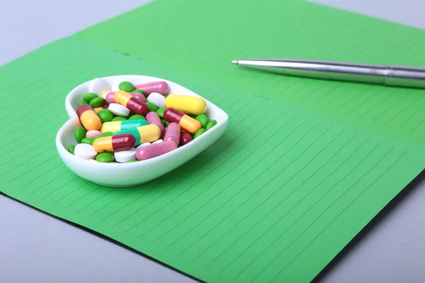 Notebook e pílulas variadas coloridas, cápsulas na placa . — Fotografia de Stock