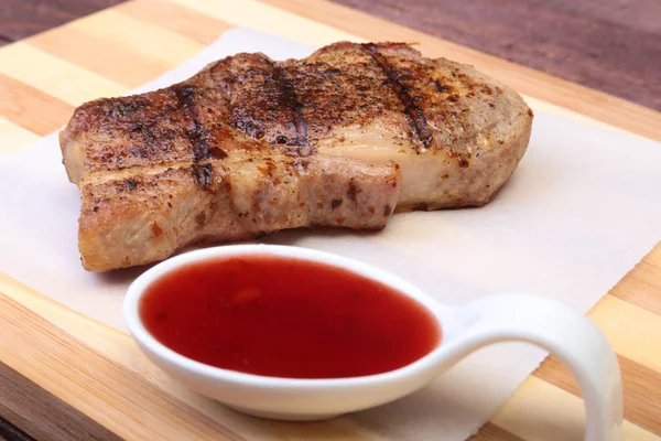 Braciola di maiale alla griglia con salsa di mirtilli rossi su tavola di legno — Foto Stock