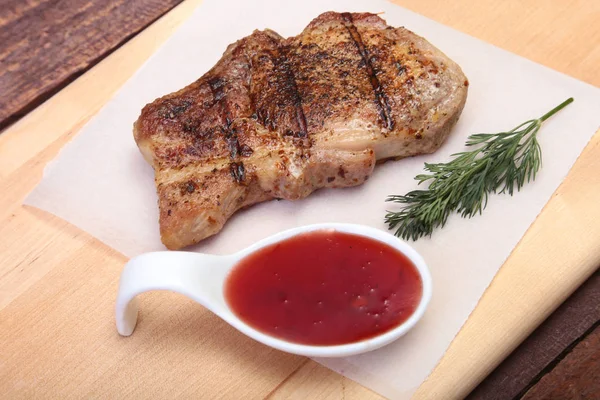 Chuleta de cerdo a la parrilla con salsa de arándano en plato sobre tabla de madera — Foto de Stock