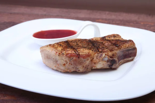 Chuleta de cerdo a la parrilla con salsa de arándano en plato sobre tabla de madera — Foto de Stock