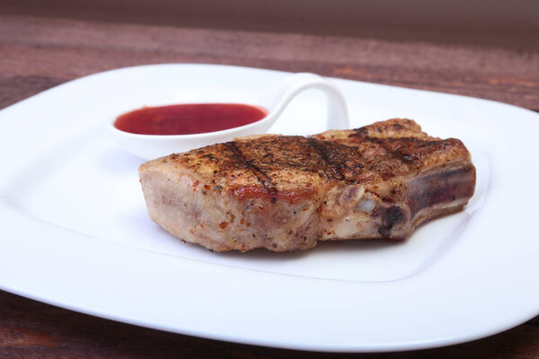 Grilled pork chop with Cranberry sauce on plate on wooden board.