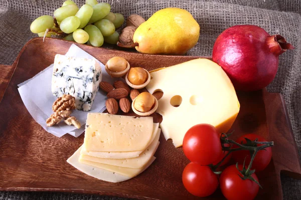 Ассортимент сыра с фруктами, виноградом и орехами на деревянном подносе . — стоковое фото