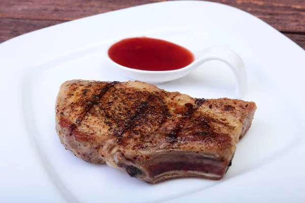 Chuleta de cerdo a la parrilla con salsa de arándano en plato sobre tabla de madera — Foto de Stock