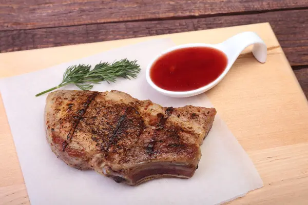 Chuleta de cerdo a la parrilla con salsa de arándano en plato sobre tabla de madera — Foto de Stock