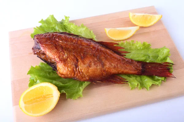 Копченая рыба и лимон на зеленых листьях салата на деревянной разделочной доске на белом фоне . — стоковое фото