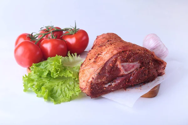 Çiğ domuz knuckle ve sebze, sarımsak, domates baharat ve marul yaprakları bir kesme tahtası üzerinde. Seçici odak. Hazır yemek pişirmek için.