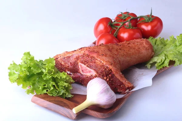 Çiğ domuz knuckle ve sebze, sarımsak, domates baharat ve marul yaprakları bir kesme tahtası üzerinde. Seçici odak. Hazır yemek pişirmek için.