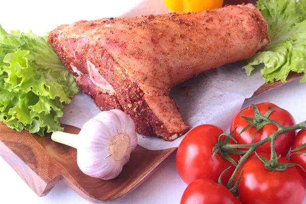 Çiğ domuz knuckle ve sebze, sarımsak, domates, dolmalık biber. baharat ve marul yaprakları bir kesme tahtası üzerinde. Seçici odak. Hazır yemek pişirmek için.