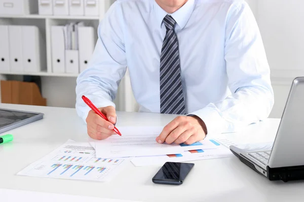 Cheerful young businessman sitting at the table in the office with laptop and looks at documents Stock Image