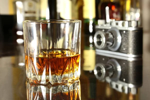 Copa de brandy o coñac y cámara retro en la mesa de madera espejo — Foto de Stock