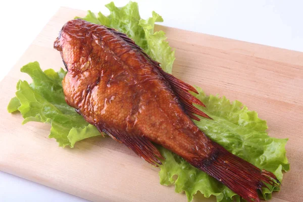 Smoked fish and lemon on green lettuce leaves on Wooden cutting board isolated on white background. — Stock Photo, Image