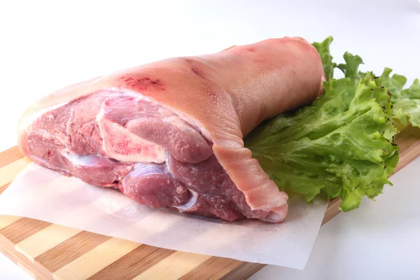 Raw pork knuckle and lettuce leaves on a cutting board. Selective focus. Ready for cooking. — Stock Photo, Image
