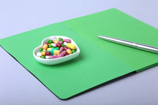 Notebook e pílulas variadas coloridas, cápsulas na placa . — Fotografia de Stock