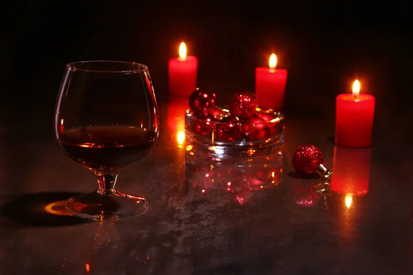 Weihnachtsdekoration. Glas Cognac oder Whiskey, rote Kerzen und bunte Kugel auf Holzgrund. — Stockfoto