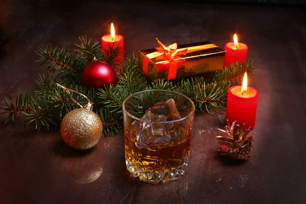 Christmas decoration with glass of cognac or whiskey, red candles, gift box and christmas tree. Selective focus. — Stock Photo, Image