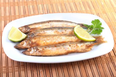 Küçük balık capelin ve beyaz tabakta dilimlenmiş limon kızartma derin. Bira için iyi snack.