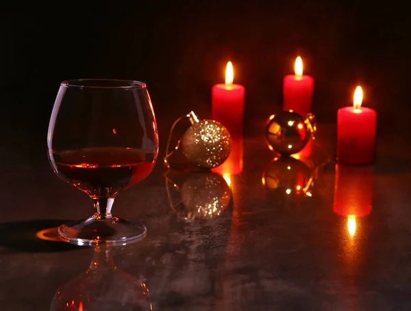 Weihnachtsdekoration. Glas Cognac oder Whiskey, rote Kerzen und bunte Kugel auf Holzgrund. — Stockfoto