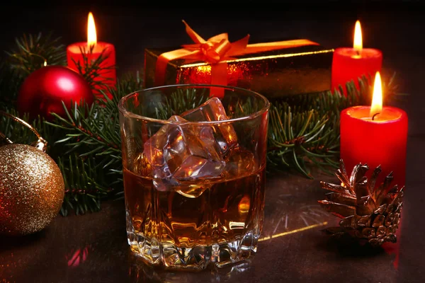 Christmas decoration with glass of cognac or whiskey, red candles, gift box and christmas tree. Selective focus. — Stock Photo, Image