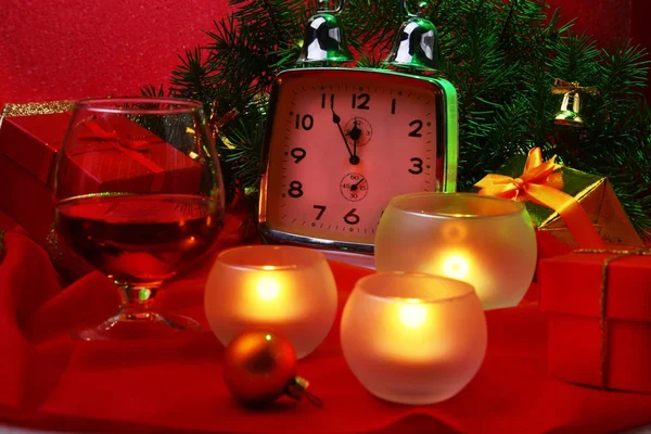 Reloj de Navidad, vaso con coñac o whisky y velas. Decoración de Año Nuevo con cajas de regalo, bolas de Navidad y árbol. Concepto de celebración para Año Nuevo . — Foto de Stock