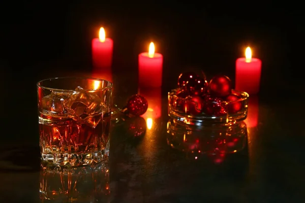 christmas decoration. glass of cognac or whiskey, christmas candles and gift box on a wooden background.