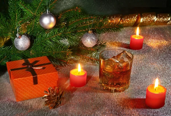 Χριστουγεννιάτικη διακόσμηση με ποτήρι ουίσκι ή κονιάκ, κεριά Χριστουγέννων, δέντρο και δώρο κουτί σε ένα αστραφτερό φόντο. Το νέο έτος διακόσμηση. — Φωτογραφία Αρχείου