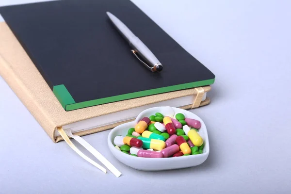 Notebook și sortimente colorate pastile, capsule pe placă . — Fotografie, imagine de stoc