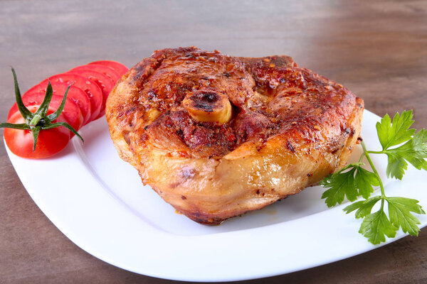 grilled pork chop with sliced tomato and sauce on wooden table.