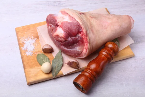 Jarret de porc cru, feuilles de laurier séchées aromatiques, ail, sel de mer, moulin à poivre et épices sur une planche à découper. Concentration sélective. Prêt pour la cuisson . — Photo