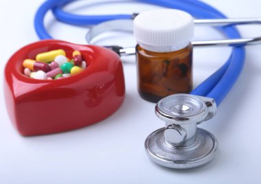 Kırmızı kalp, asorted pils ve beyaz arka plan üzerinde bir stetoskop.