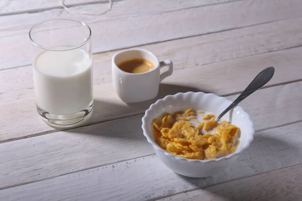 Corn Flakes cereal in a bowl, glass with milk and cap with espresso coffee. Morning breakfast.