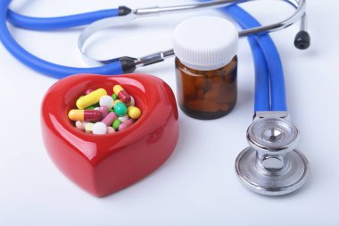 Kırmızı kalp, asorted pils ve beyaz arka plan üzerinde bir stetoskop.