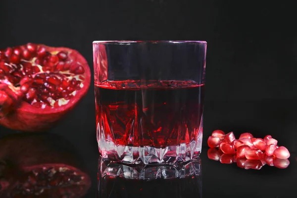 Vidro com suco de romã Sementes de romã e romã madura bonita no fundo do espelho preto com lugar para espaço de cópia . — Fotografia de Stock