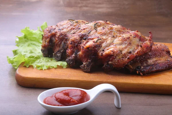 Grilled barbecued ribs with lettuce leaves, hot chili pepper and sauce on wooden cutting board. — Stock Photo, Image