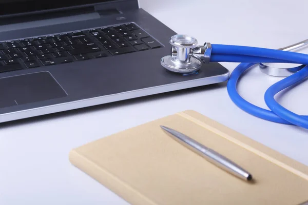 Workplace of doctor with laptop, stethoscope and notebook on white table. Copy space.