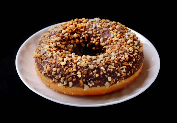 Assorted doughnuts in the glaze, colorful sprinkles and nuts on a black background. — Stock Photo, Image