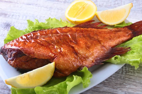 Poisson fumé et citron sur feuilles de laitue verte sur planche à découper en bois isolée sur fond blanc . — Photo