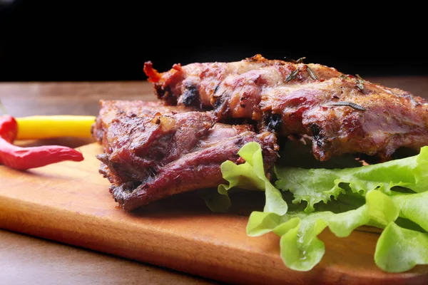 Iga panggang panggang dengan daun selada, cabai pedas dan saus di papan potong kayu . — Stok Foto