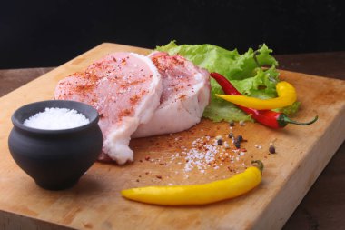 Çiğ biftek, pirzola rustik kesme tahtası ile tuz, biber ve baharat değirmeni. Kopya alanı için siyah arka plan. Üstten Görünüm.