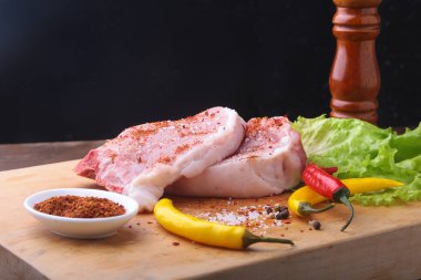 Çiğ biftek, pirzola rustik kesme tahtası ile tuz, biber ve baharat değirmeni. Kopya alanı için siyah arka plan. Üstten Görünüm.