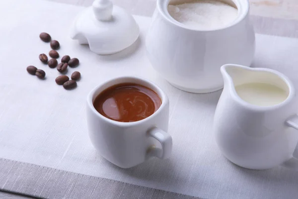 Cup of hot coffee espresso, coffee beans, jug of milk, and bowl with sugar on white background for copy space. Coffee concept.