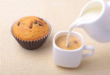 Sabah kahvaltı lezzetli ev yapımı kekler kuru üzüm, çikolata parçaları, espresso kahve beyaz Kupası ve Tekstil arka plan üzerinde süt ile mükemmel. Muffins.