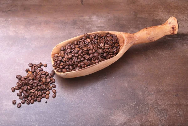 Granos de café en una cucharada de madera en la mesa de piedra oscura . — Foto de Stock