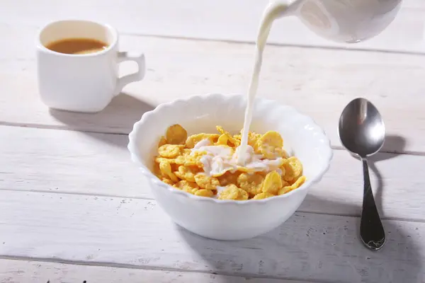 Milk pouring into a bowl of delicious corn flake cereals and cap with espresso coffee. Morning breakfast. — Stock Photo, Image
